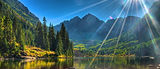 Green pine trees with large mountains in the background and sun rays shining down